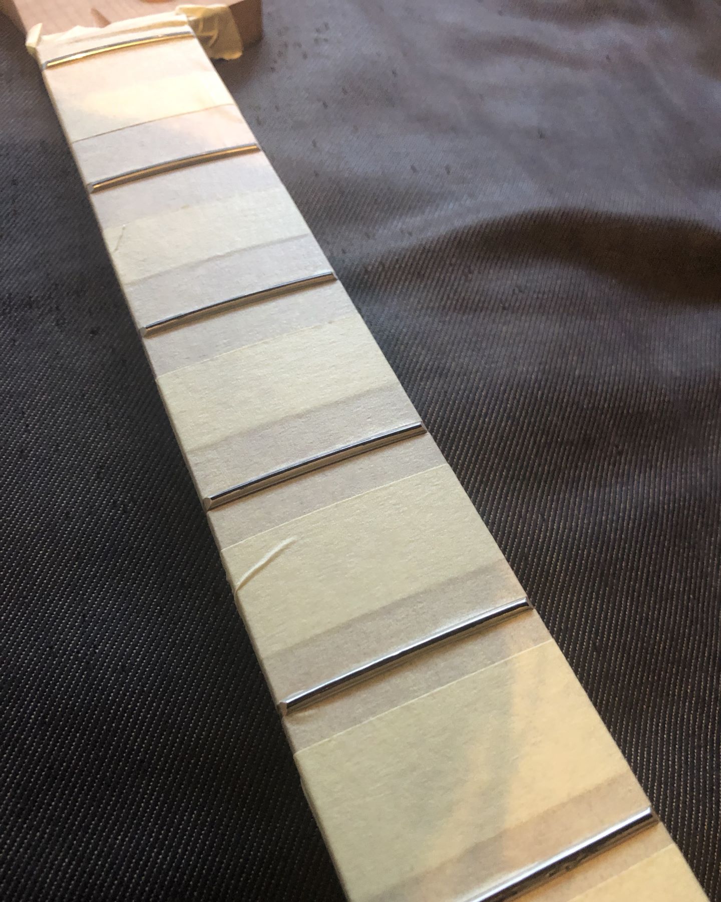 Photo of the middle section of the fretboard of a bass guitar neck covered in masking tape between the frets.