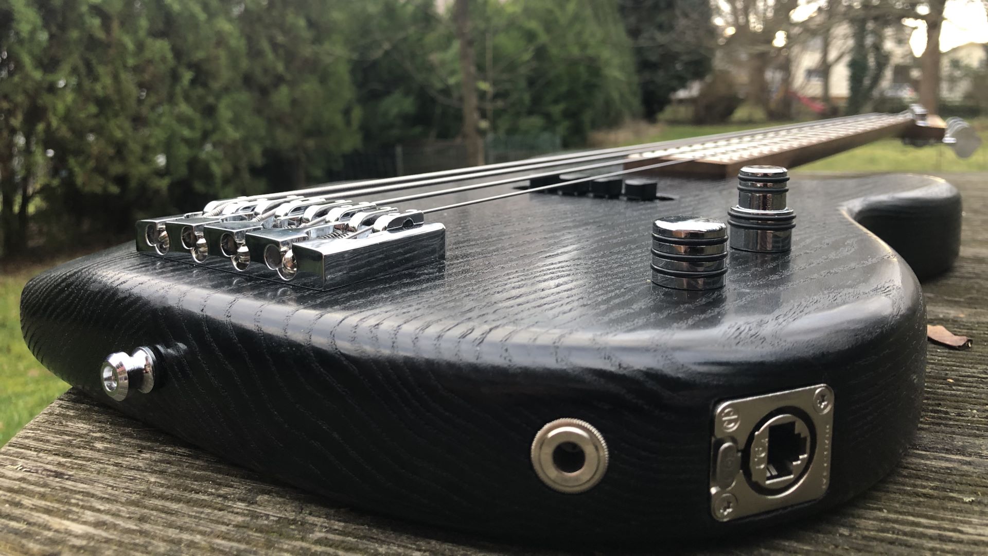 Low-angle photo from slightly above the side jacks of a finished bass guitar. The chrome-plated hardware is installed. The bass has two control knobs, one regular, one stacked.
